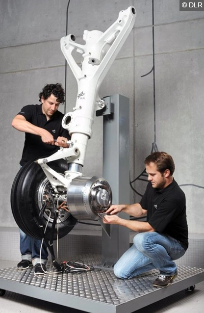 Ein Foto von zwei Mechanikern die an dem Elektrischen Bugrad, aufgebaut auf einem Ständer schrauben. 